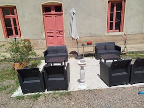 An outdoor seating area with wicker furniture, a white pedestal table, and a red door in the background. - 18TH-CENTURY CLAIREFONTAINE GARCHIZY CASTLE (Garchizy)