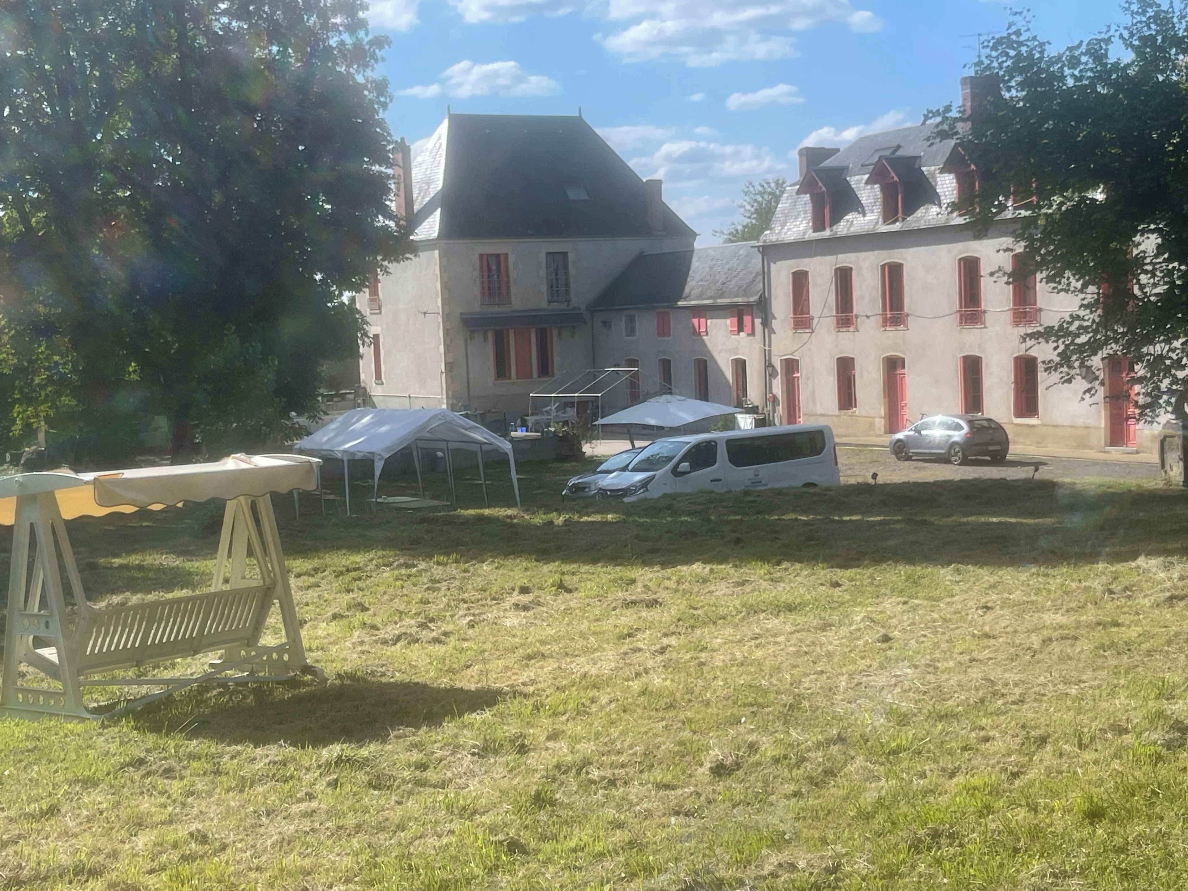 Une cour avec une tente, un fourgon blanc et un bâtiment aux fenêtres rouges.