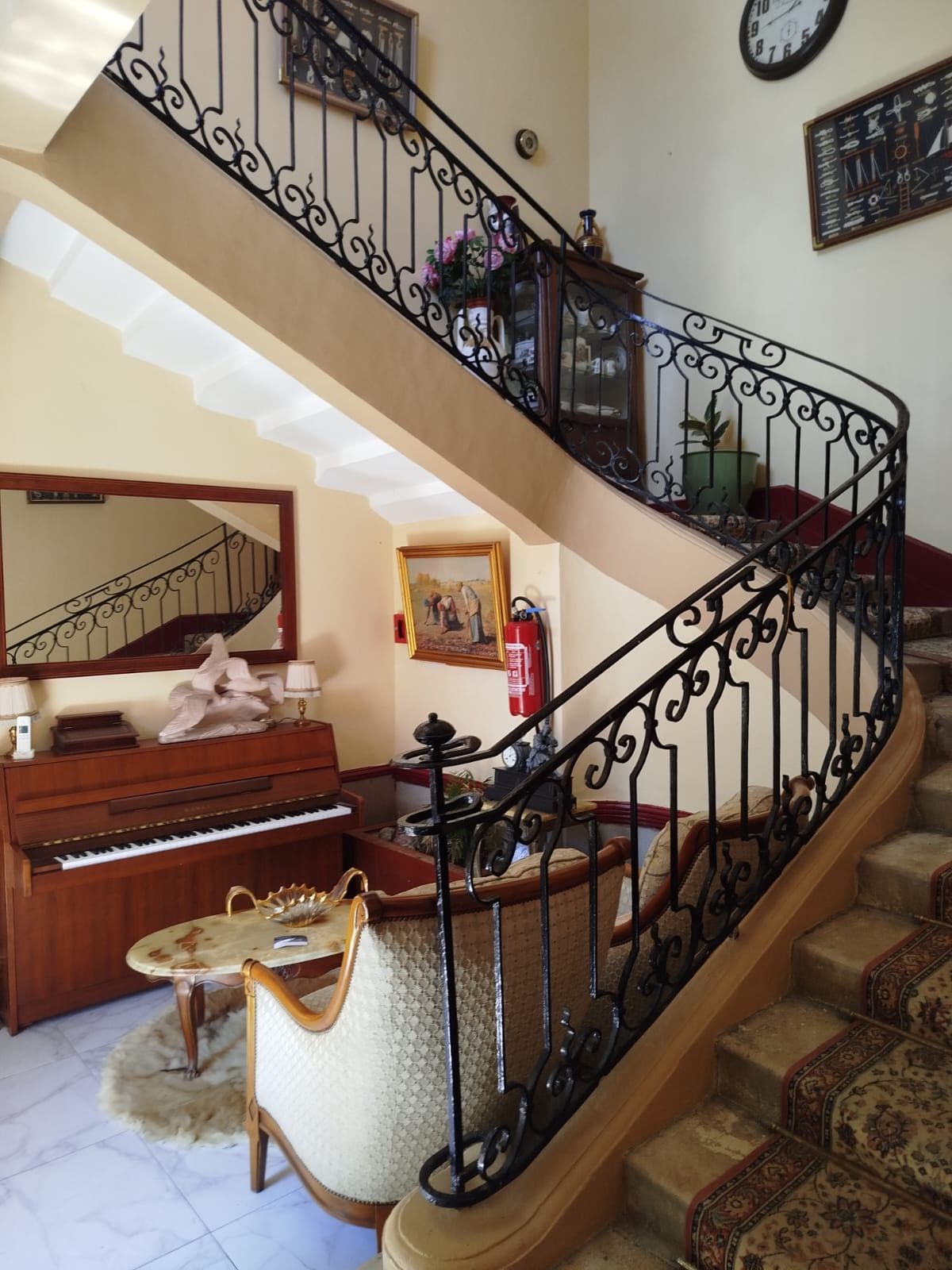 Un magnifique escalier orné de rampes noires, un piano, un canapé et un miroir.