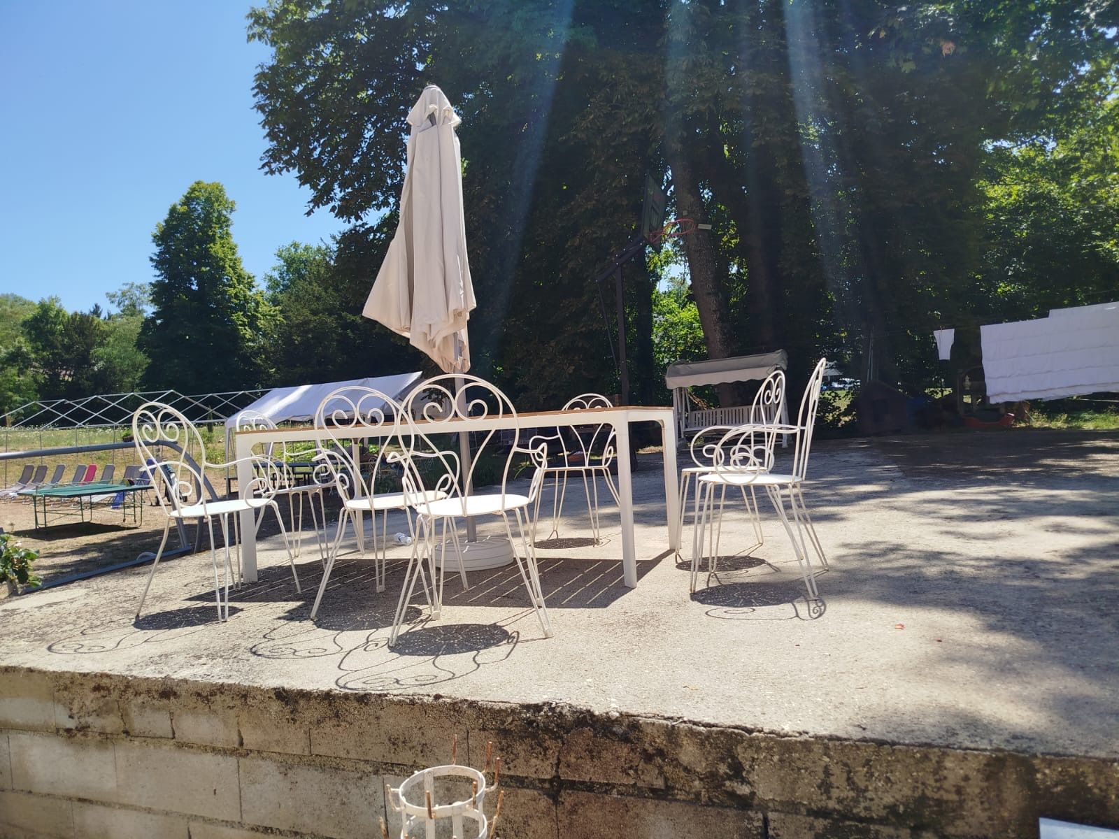 Ein Sitzbereich im Freien mit Metallstühlen und einem Tisch, umgeben von Bäumen.