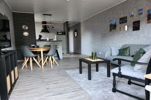 A modern living room with a grey sofa, a dining table with chairs, and a kitchen area in the background. - Kriemhild's Dragon's Cave (Xanten)