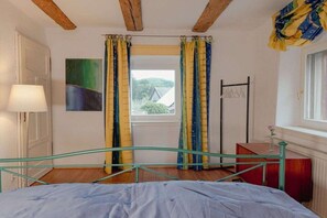 Ein Schlafzimmer mit Bett, Fenster mit Vorhängen, Nachttisch und Lampe.