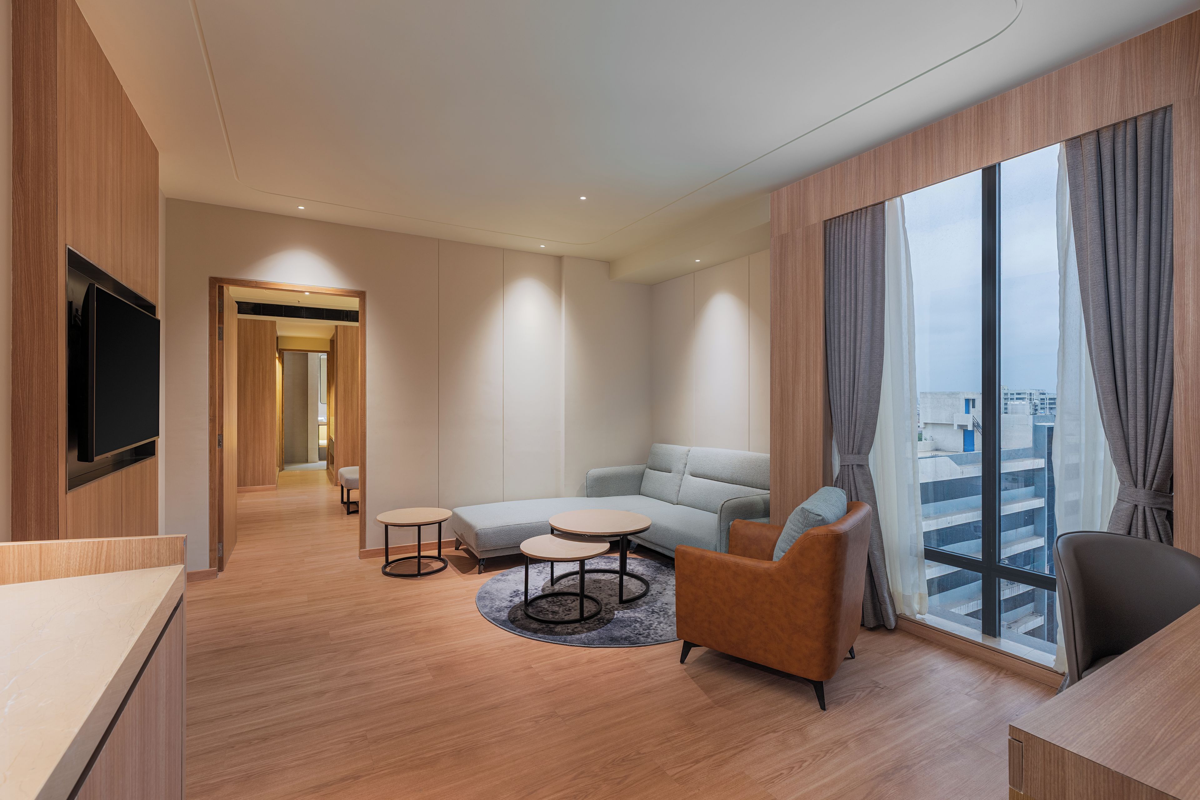 Una habitación de hotel moderna con sofá, sillones, una pequeña mesa y un televisor montado en la pared.