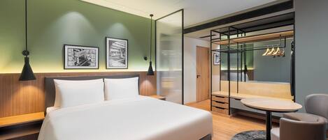 Una habitación de hotel moderna con una cama grande, una zona de estar con una mesa y un armario con ropa colgada.