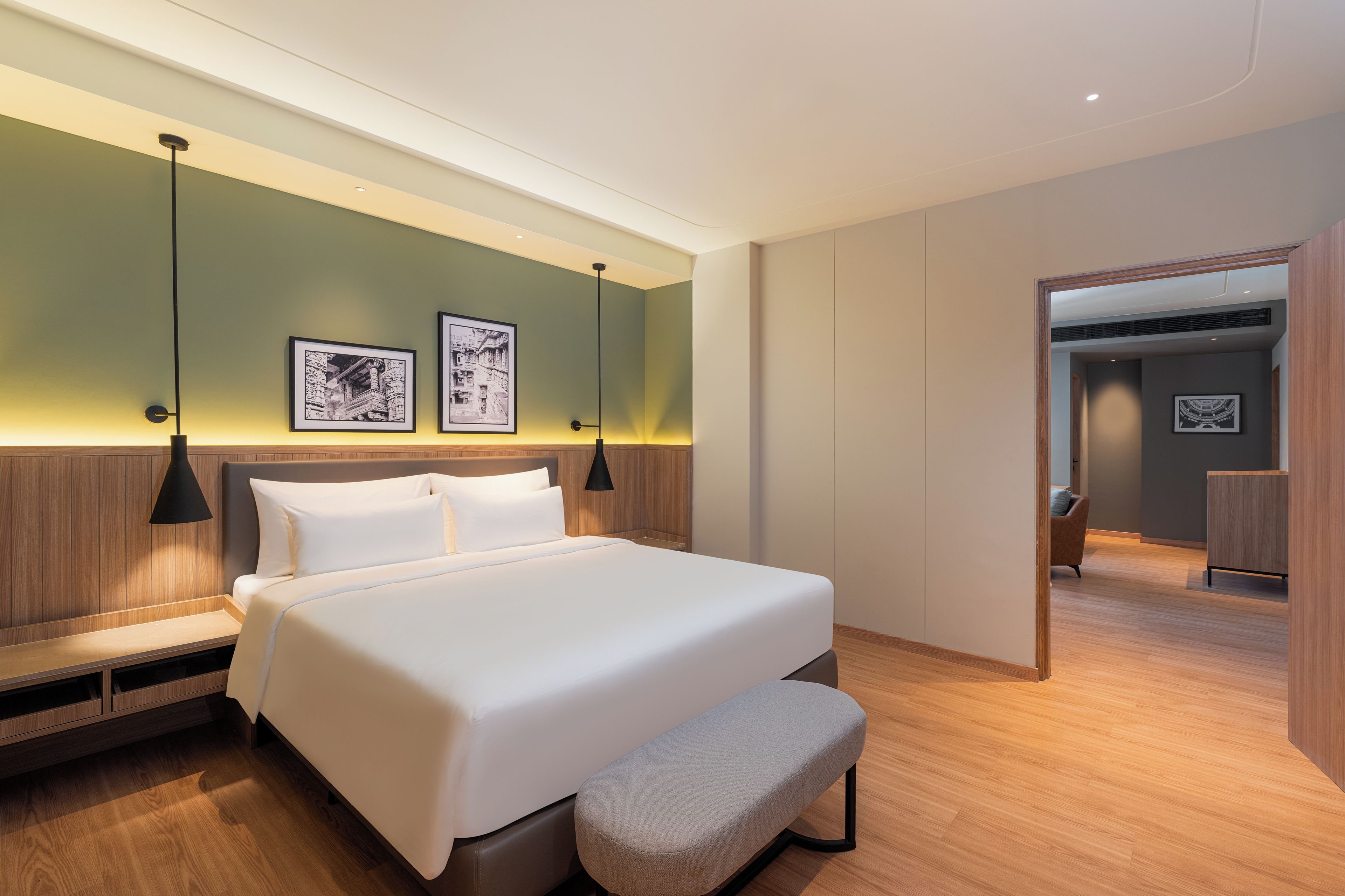 A modern hotel room with a large bed, bedside tables, a bench, and artwork on the walls.