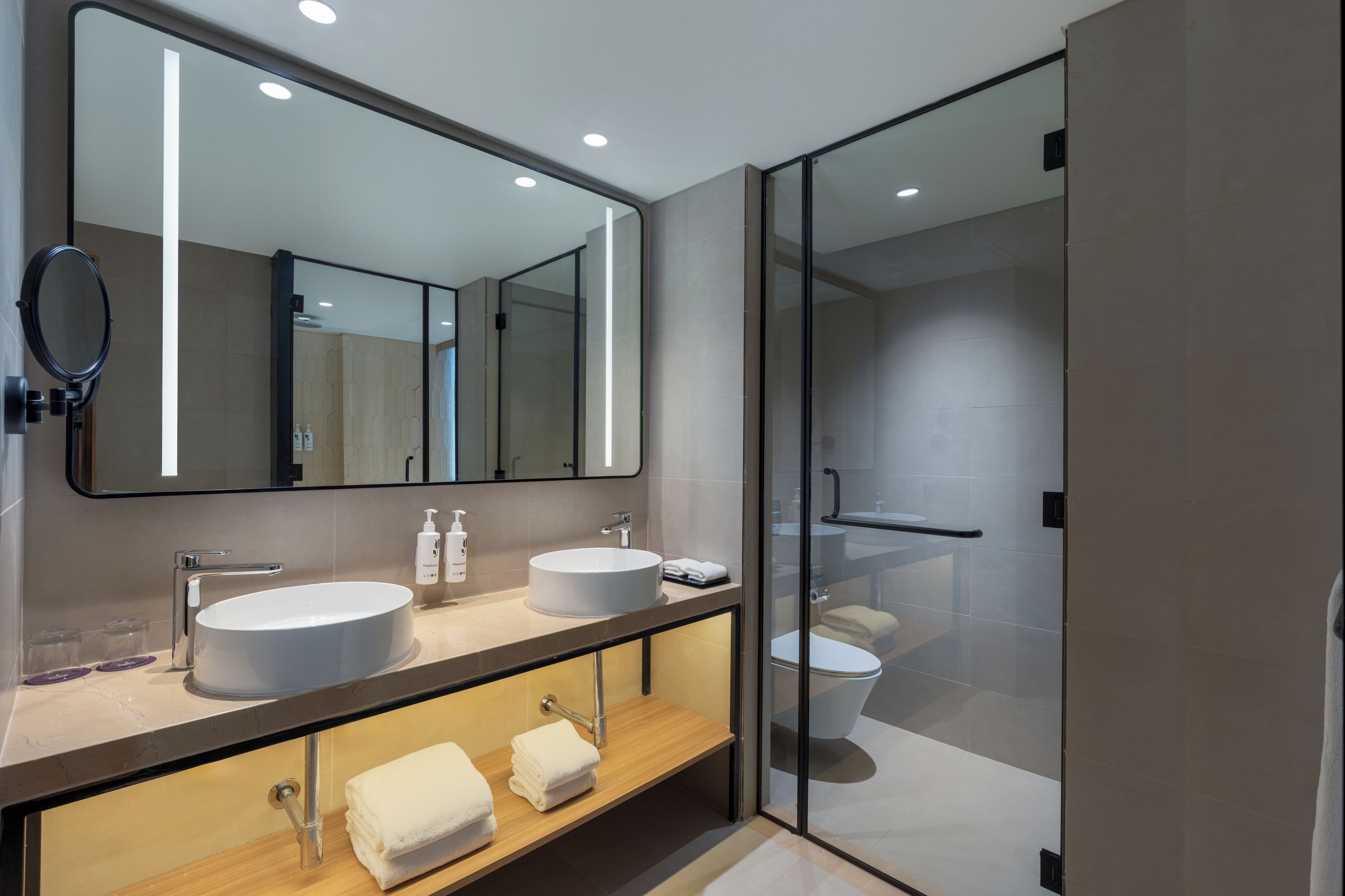Une salle de bain moderne avec un grand miroir, deux vasques et une douche à l’italienne.