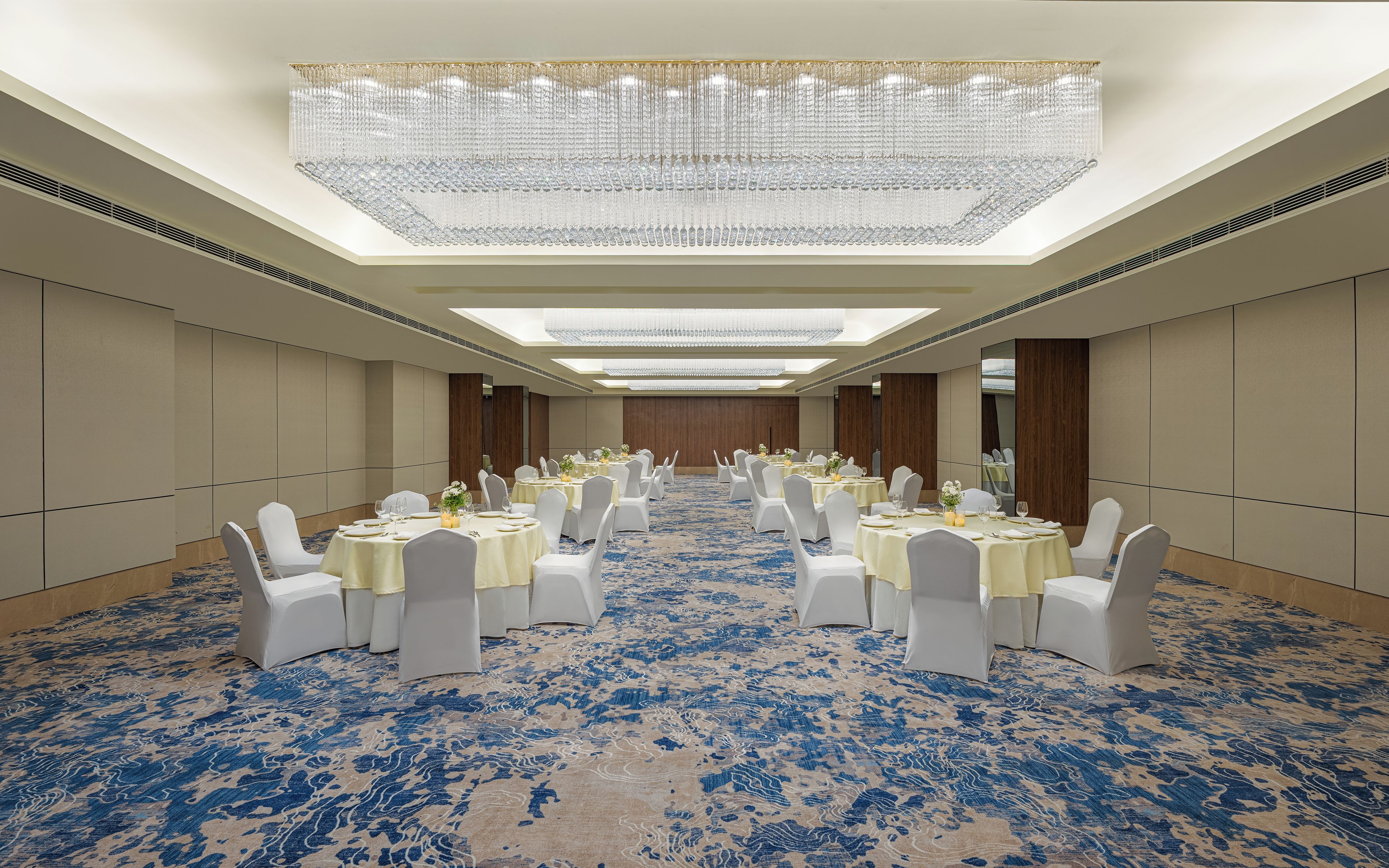 Une salle de conférence avec des tables rondes, des chaises blanches et un tapis bleu à motifs.
