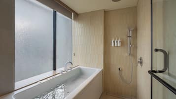 A modern bathroom with a bathtub, shower, and a window.