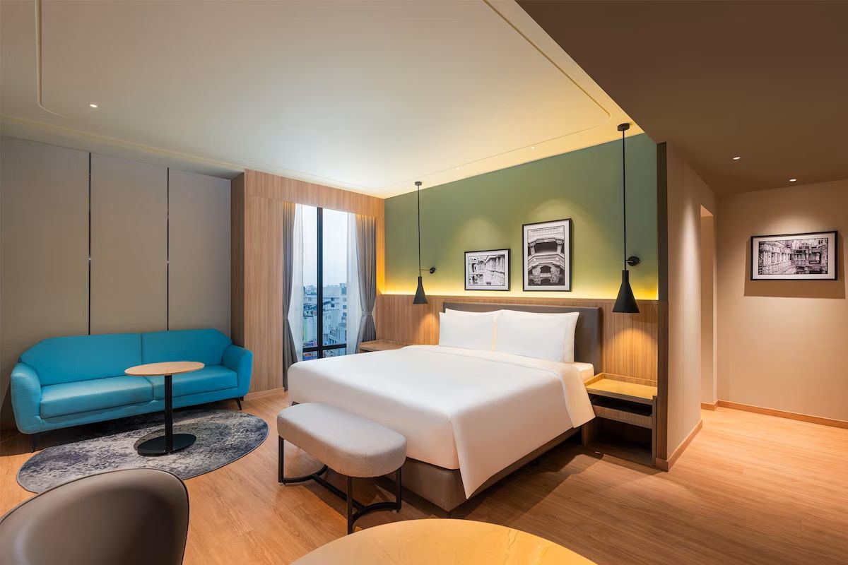 A modern hotel room with a bed, a blue sofa, a small table, and a bench.