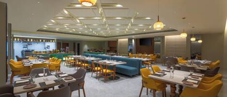 Un restaurante moderno con varias áreas de comedor, que incluyen un bar y una zona de estar con un sofá azul.