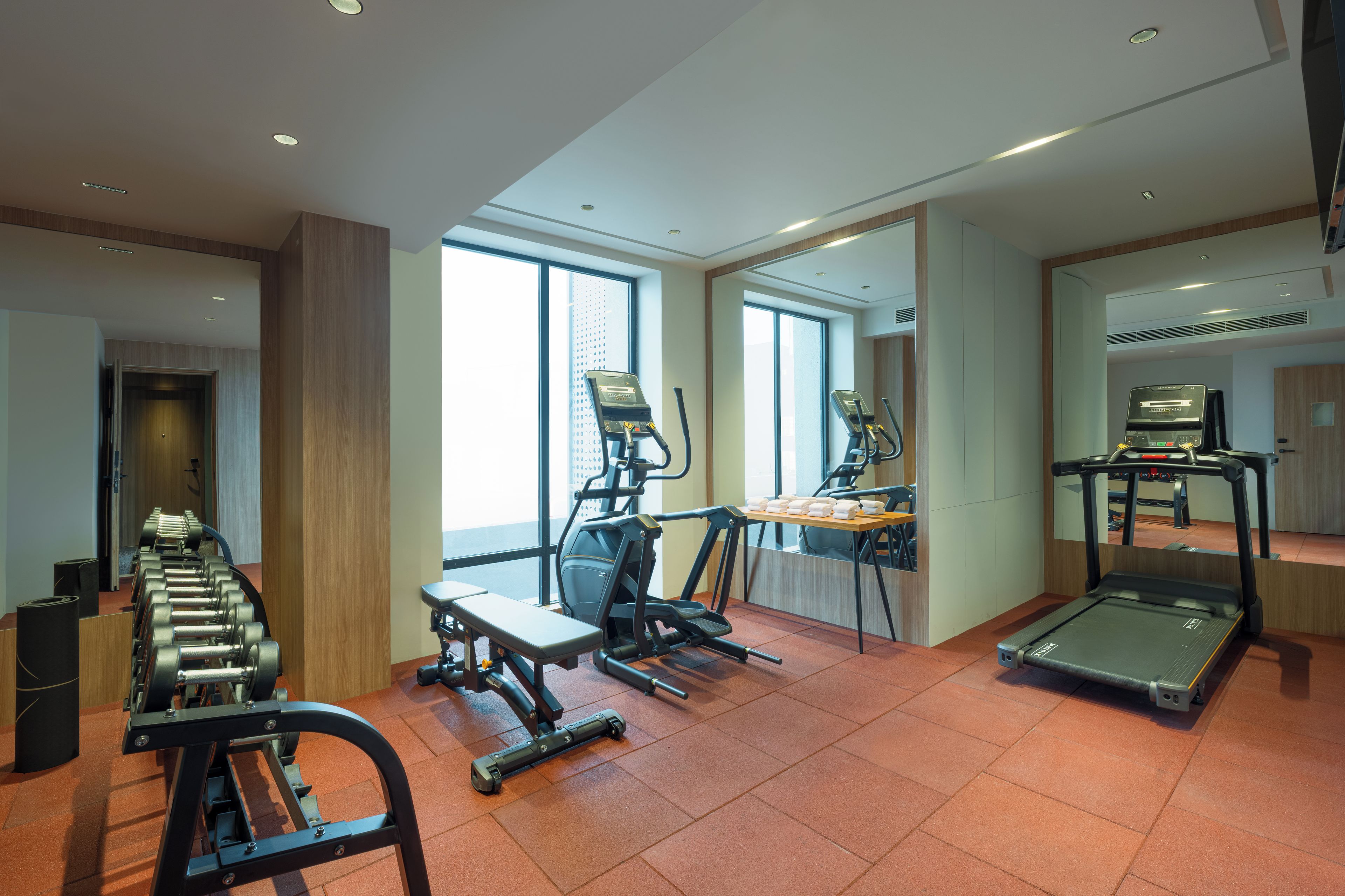 Un gimnasio con equipo de ejercicio, ventanas amplias y un espejo.