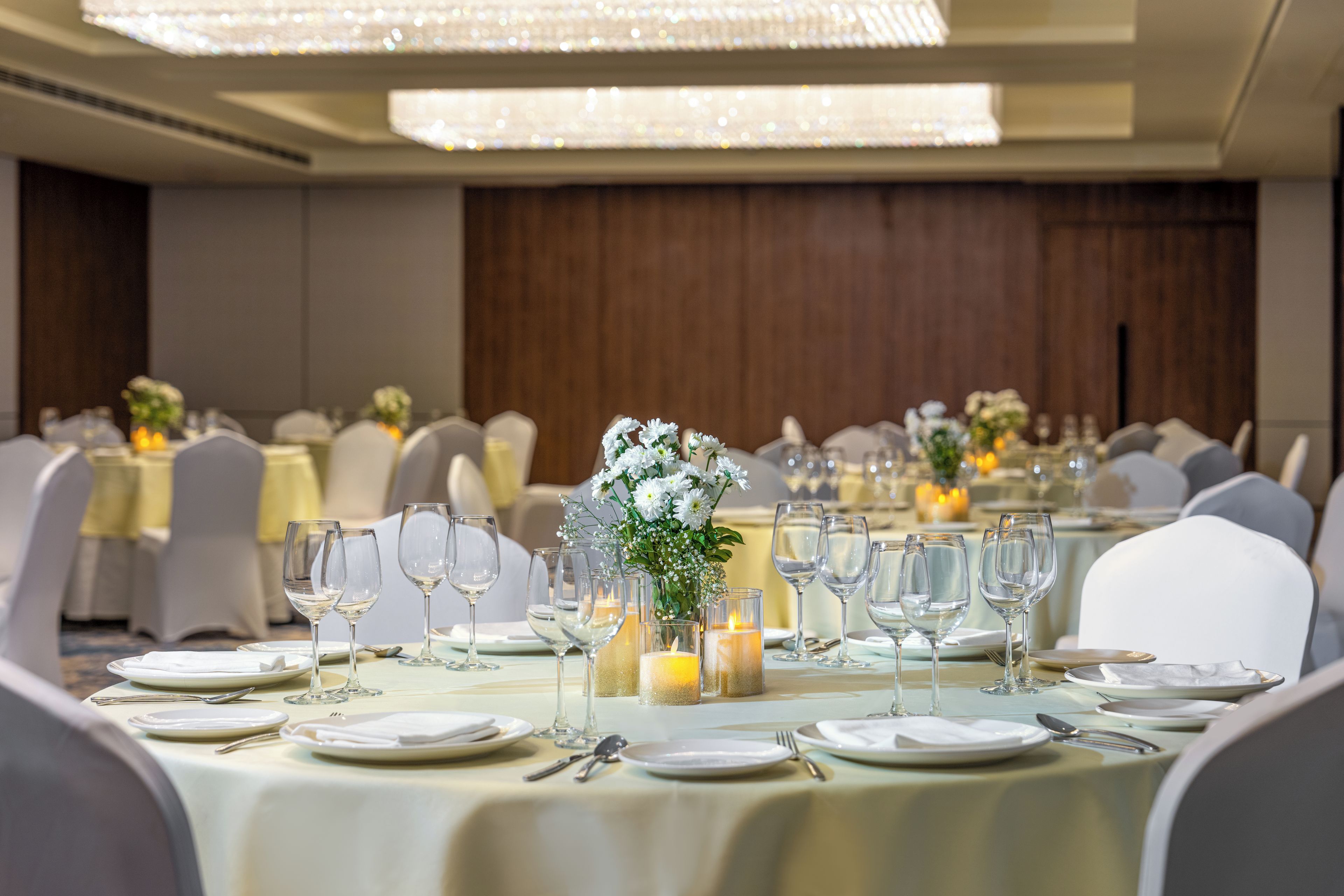 A banquet hall with round tables set for dining, each with white tablecloths, glassware, and candles.