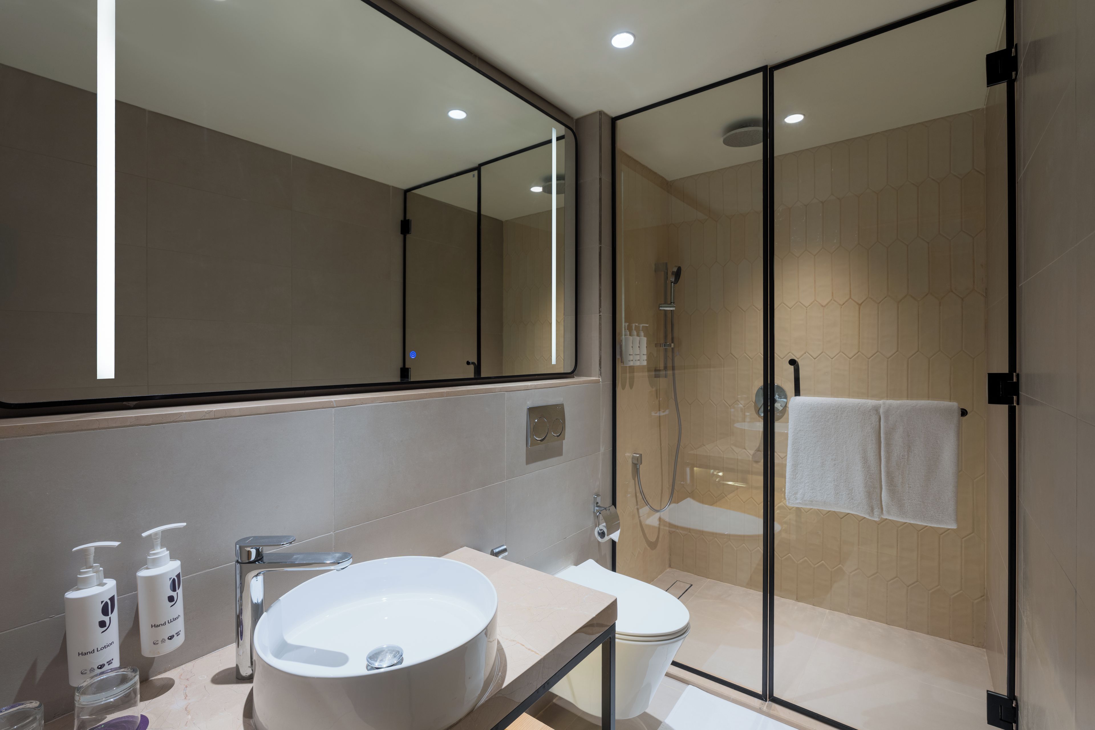 Un baño moderno con ducha envuelta en vidrio, un espejo grande y un tocador con lavamanos y artículos de aseo.