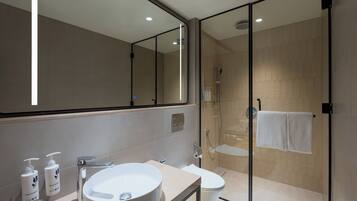Un baño moderno con ducha envuelta en vidrio, un espejo grande y un tocador con lavamanos y artículos de aseo.