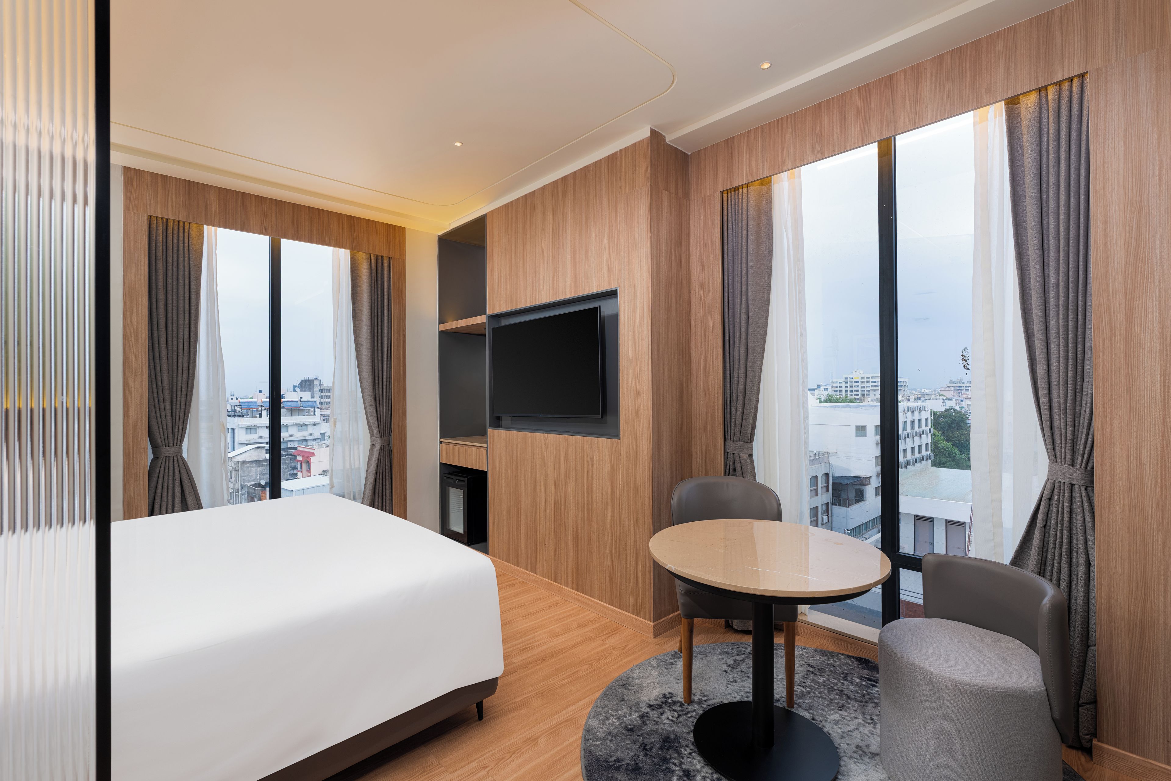 Habitación de hotel con cama, televisión, mesa de comedor y vistas a la ciudad.