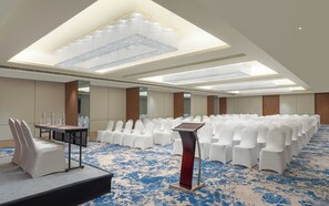 Un salón de conferencias con filas de sillas blancas, un atril y una gran lámpara de candelabro.