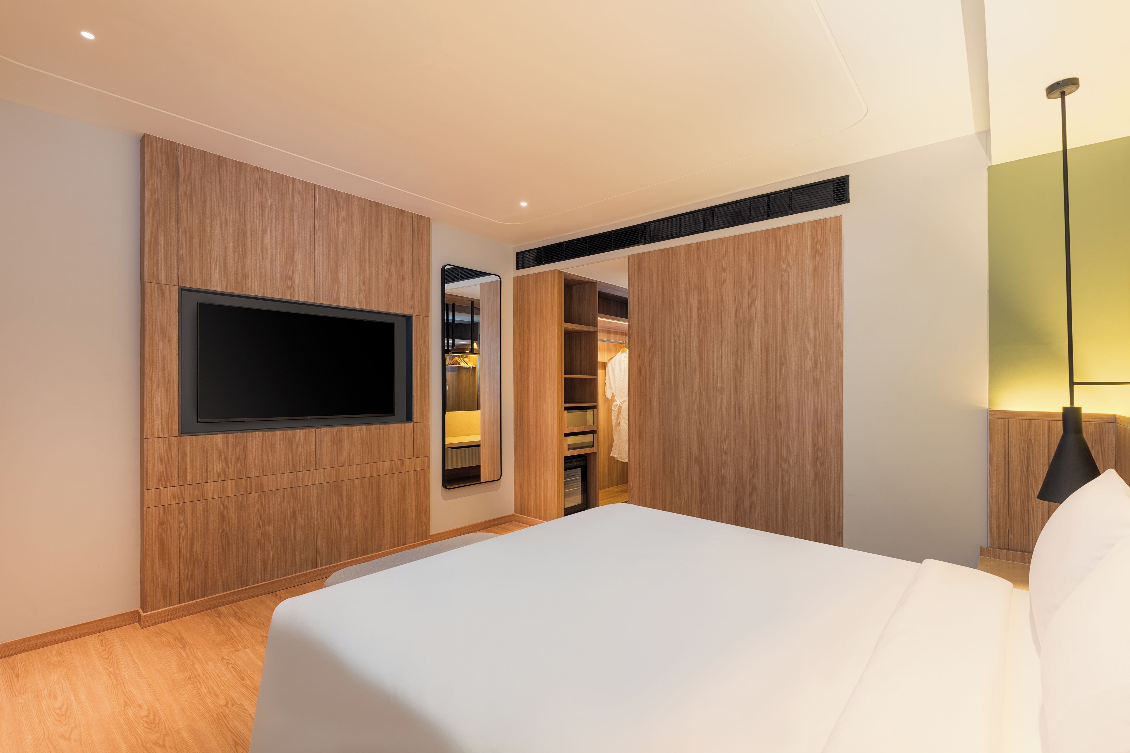 A hotel room with a bed, a TV mounted on the wall, a wardrobe, and a mirror.