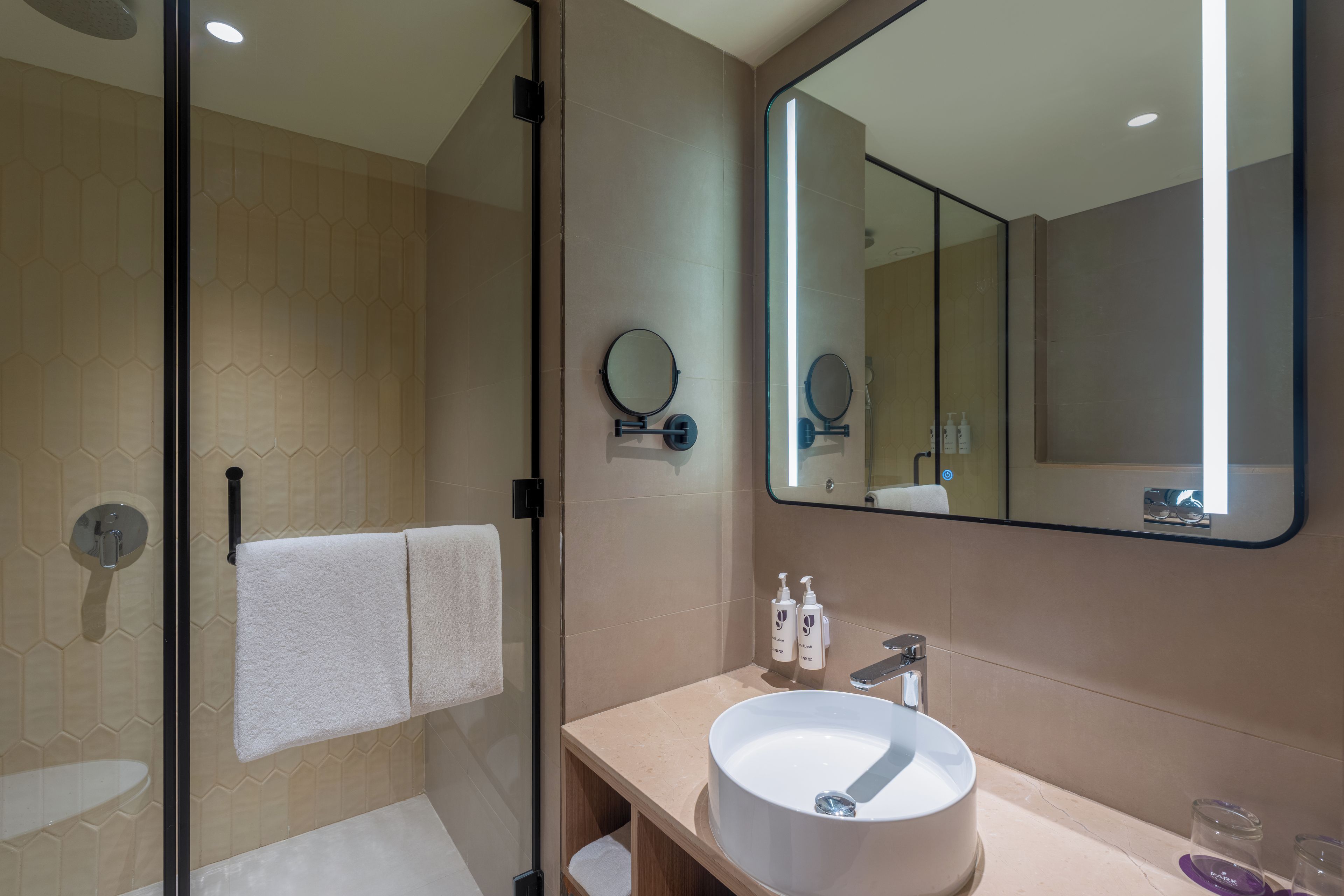 A modern bathroom with a glass shower enclosure, a round sink, and a large mirror.