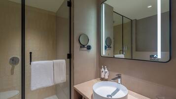 A modern bathroom with a glass shower enclosure, a round sink, and a large mirror.