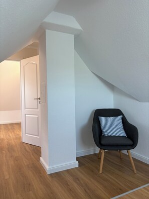 A room with a sloped ceiling, a white door, a black chair with a striped pillow, and wooden flooring. - Inselruhe - Ihre Auszeit auf Fehmarn (Fehmarn)