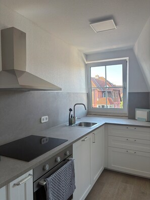 A modern kitchen with a built-in stove, oven, and a window with a view of a red-roofed building. - Inselruhe - Ihre Auszeit auf Fehmarn (Fehmarn)