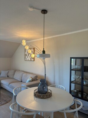 A modern living room with a white round table, a decorative vase, and a unique ceiling light fixture. - Inselruhe - Ihre Auszeit auf Fehmarn (Fehmarn)
