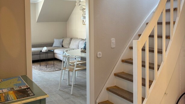 A staircase leading to an upper level, a dining area with a table and chairs, and a living room with a sofa and a rug. - Inselruhe - Ihre Auszeit auf Fehmarn (Fehmarn)