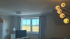 A living room with a television, sofa, and a view of a field through the window. - Inselruhe - Ihre Auszeit auf Fehmarn (Fehmarn)