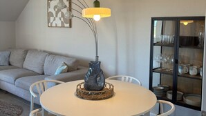 A dining area with a round table, white chairs, a decorative vase, and a modern pendant light. - Inselruhe - Ihre Auszeit auf Fehmarn (Fehmarn)