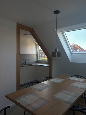 A dining area with a wooden table, chairs, a hanging light fixture, and a view through a skylight. - Inselruhe - Ihre Auszeit auf Fehmarn (Fehmarn)