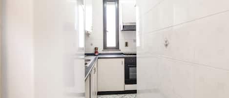 Una cocina estrecha con paredes de azulejos blancos y piso de losetas negras.