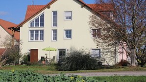 Een gebouw met twee verdiepingen, een rode pannendak, meerdere ramen en een deur met een groene parasol ervoor.