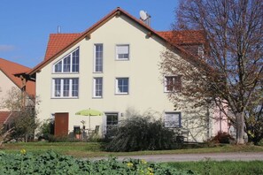 A two-story building with a red-tiled roof, multiple windows, and a door with a green umbrella in front. - Holiday apartment with 2 bedrooms (Mühlhausen-Ehingen)