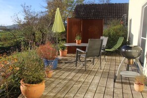 An outdoor patio with a table and chairs, surrounded by potted plants and a barbecue grill. - Holiday apartment with 2 bedrooms (Mühlhausen-Ehingen)