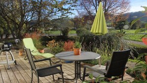 Een terras buiten, met een ronde tafel en stoelen, omgeven door plantenpotten en uitzicht op een landschap.