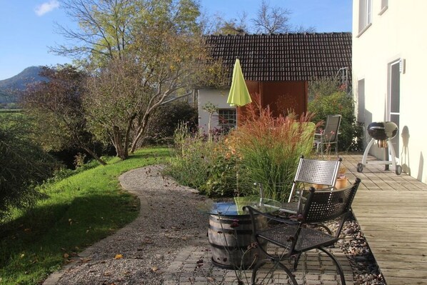 A patio with a table and chairs, a barrel, and a small shed with a green umbrella. - Holiday apartment with 2 bedrooms (Mühlhausen-Ehingen)