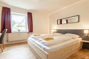 A hotel room with a bed, a chair, a window with curtains, a radiator, and a wall-mounted mirror.