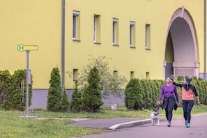A building with a yellow facade, a pedestrian pathway, and two individuals walking a dog.