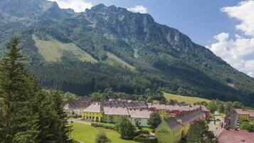 A mountain village with traditional buildings, a central green-roofed structure, and a backdrop of rugged mountains.