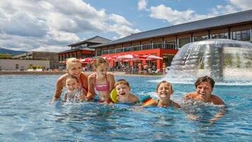 A swimming pool with people in it, a building with a red facade, and a water feature.