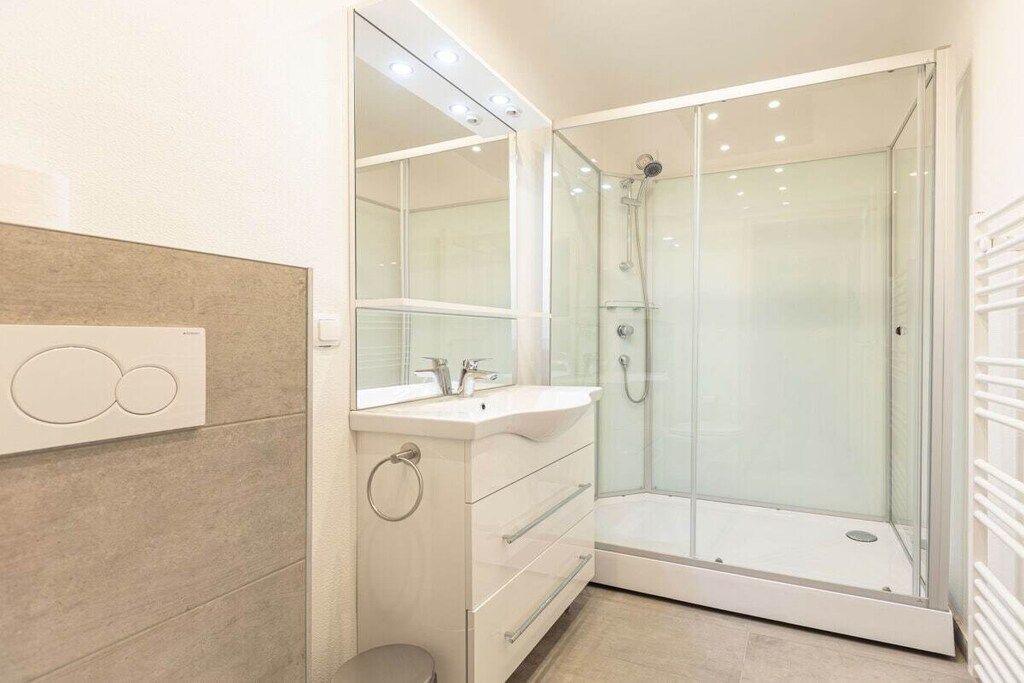 Ein modernes Badezimmer mit einer Duschkabine aus Glas, einem Waschtisch mit Spiegel und einer Toilette.