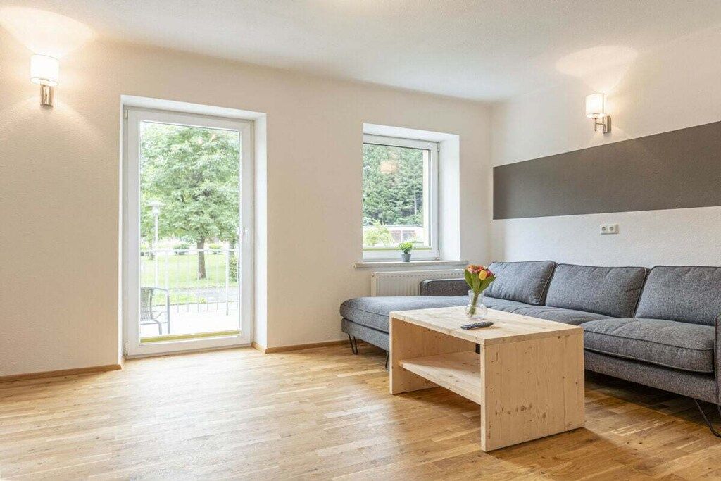 A modern living room with a sofa, a coffee table, and a view through a large window.