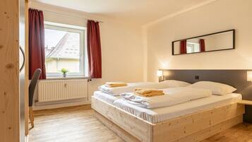 Une chambre à coucher avec un lit en bois, une fenêtre avec des rideaux, un radiateur et un miroir au mur.