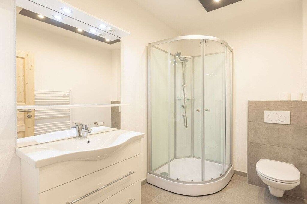 A modern bathroom with a glass-enclosed shower, a white sink with a mirror, and a toilet.