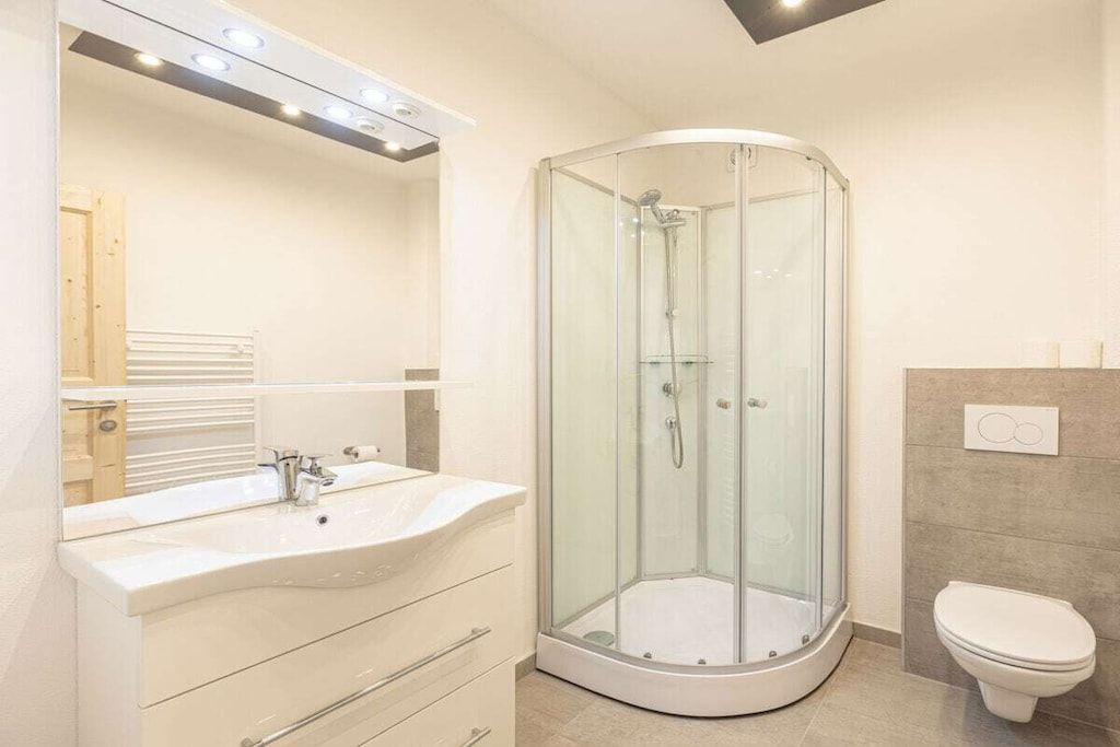 Ein modernes Badezimmer mit einer Duschkabine, einem weißen Waschbecken und einer Toilette.