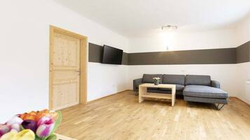 Ein Zimmer mit Holztür, einem grauen Sofa, einem kleinen Tisch und einem an der Wand befestigten Flachbildfernseher.