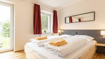 A bedroom with two beds, a window with curtains, a mirror, and a bedside table.
