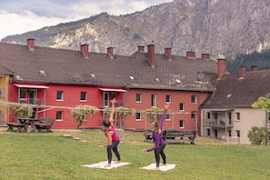 Two individuals practicing yoga on mats in an outdoor setting with a building and mountains in the background.