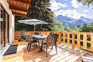 An outdoor deck with a table and chairs, a wooden fence, and a view of mountains. - Cabin in Annaberg with swimming pool (Annaberg)