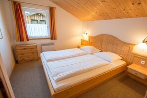 Une chambre avec un lit en bois, deux tables de chevet, une fenêtre avec des rideaux et un radiateur.